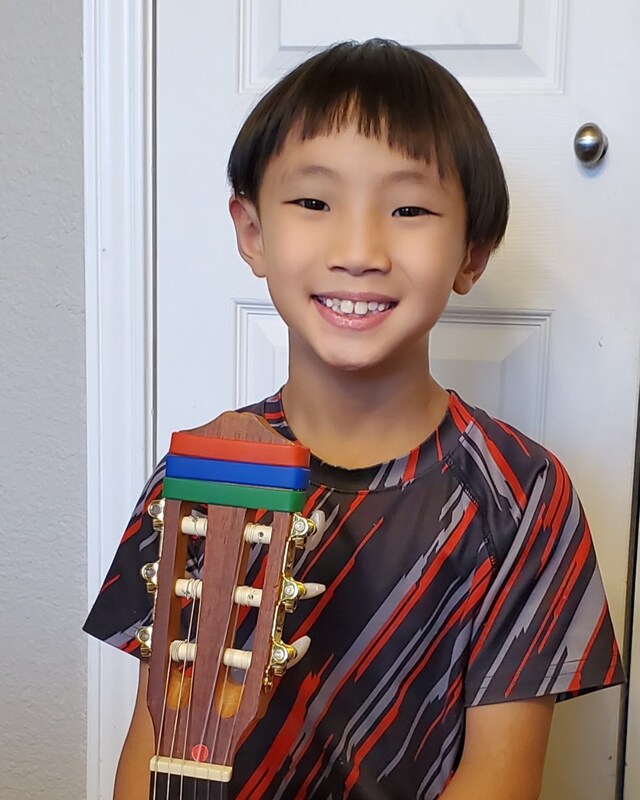 Student smiling and showing his three different bracelets on his guitar