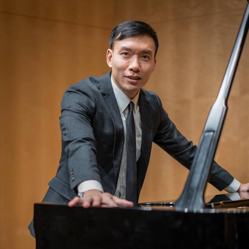Benjamin Wong standing at piano with arms outstretched