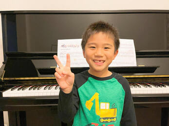 Student smiling and showing peace sign at piano