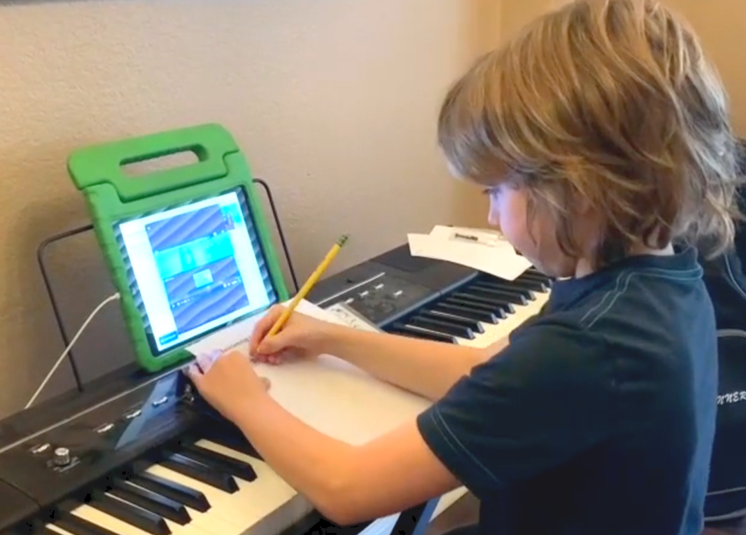 a piano student writing music and following video on iPad