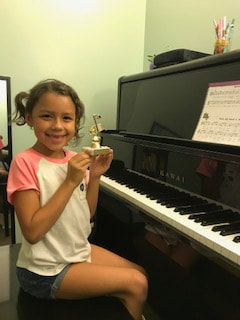 Student holding a trophy at the piano and smiling