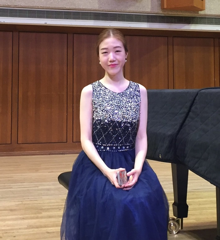 Jae Eun Baek sitting at piano in concert dress