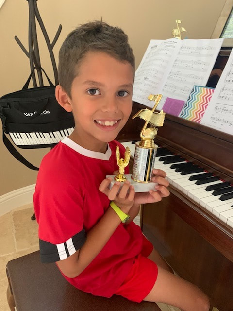 young boy with trophy sitting at the piano