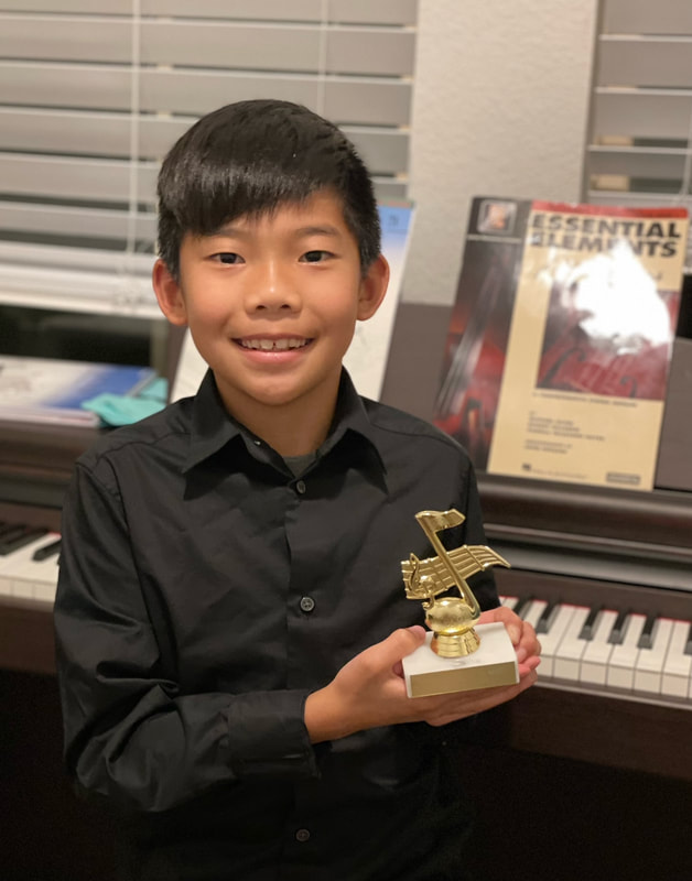 young student dressed up and holding trophy in front of piano