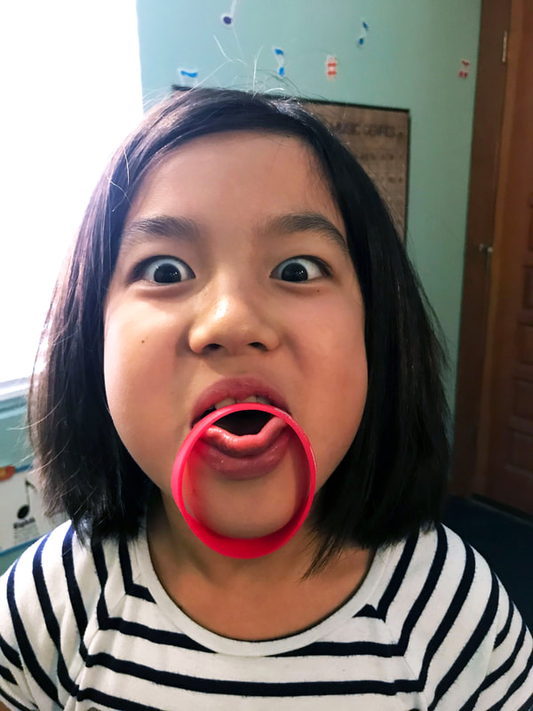 Student balancing red bracelet on her tongue